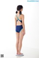 A woman in a blue and black one piece swimsuit standing on a scale.